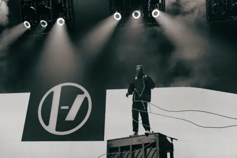 Tyler Joseph z Twenty One Pilots na scenie w Łodzi, w charakterystycznym stroju, na tle logo zespołu.