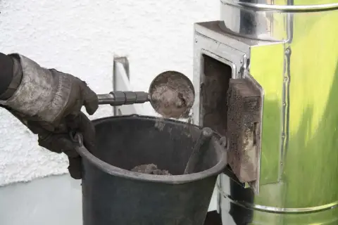 Rękawica zrzuca sadzę do wiadra. Czyszczenie komina od dołu to ważny etap dbania o bezpieczeństwo.