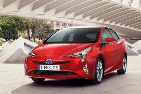 Czerwony Prius 4 z nowoczesnym designem, zaparkowany pod betonową konstrukcją z palmami w tle.