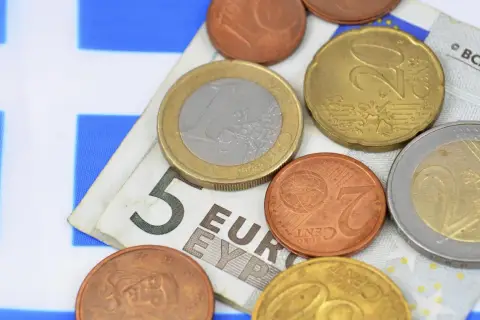 Euro to waluta w Grecji. Monety i banknot 5 euro na tle greckiej flagi.