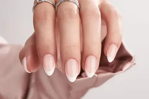 En hand med eleganta, korta french naglar och två glittrande ringar.