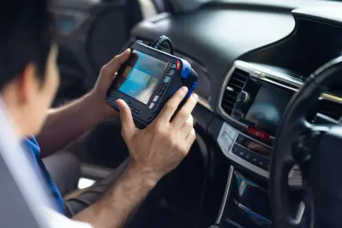 Mechanik trzymający w samochodzie urządzenie diagnostyczne podłączone do deski rozdzielczej.