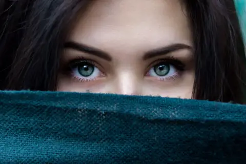 Ojos verdes penetrantes, enmarcados por cabello oscuro y un pañuelo. Un vistazo a la belleza que el microblading puede realzar.
