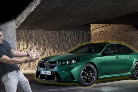 Mężczyzna z entuzjazmem prezentuje zielone BMW G90 pod betonowym zadaszeniem.