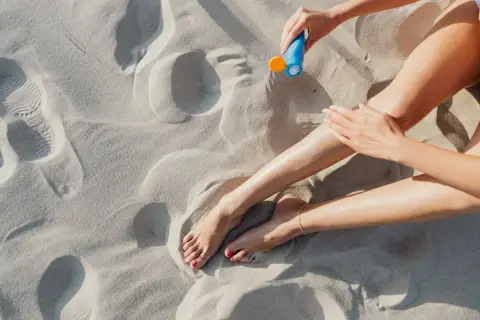 Kobieta smaruje nogi kremem z filtrem zawierającym ethylhexyl methoxycinnamate na piaszczystej plaży.