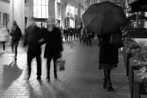 Nocne street photography. Rozmyte postacie spieszą się ulicą, jedna osoba z parasolką.