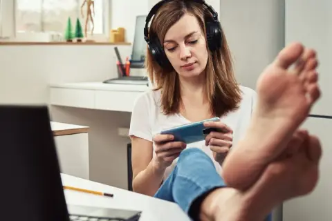 Kobieta w słuchawkach gra na telefonie, nogi na biurku. Czy to prokrastynacja co to?