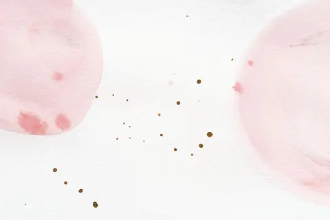 Sanfte Aquarellkreise in Rosa und Weiß mischen sich. Kleine goldene Tupfer verteilen sich auf dem Papier.