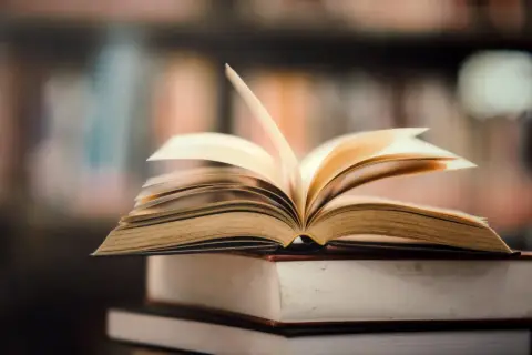 Otwarta książka na stosie innych. Idealne miejsce, gdzie oddać książki za darmo, to biblioteka lub punkt wymiany.