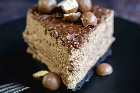 Une part de gâteau au chocolat aérien, garnie de boules Malteser croquantes et d'un glaçage au chocolat.