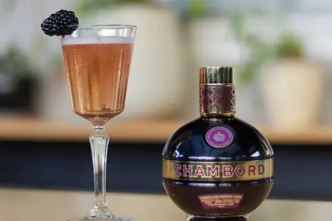 Elegancki kieliszek różowego drinka z jeżyną i butelka likieru Chambord.