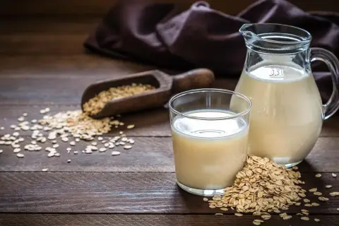 Szklanka i dzbanek z napojem owsianym Inka, obok rozsypane płatki owsiane i drewniana łyżka.