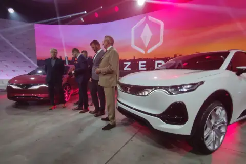 Prezentacja nowoczesnego izera samochód. Na scenie stoi biały i czerwony model, obok nich grupa mężczyzn w garniturach.