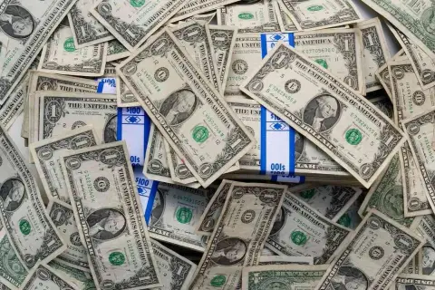 Stosy banknotów jednodolarowych i paczki z napisem "100". To obraz księgowania millenium, gdzie pieniądze odgrywają kluczową rolę.