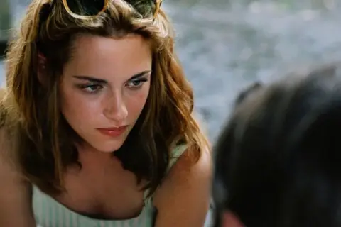 Kristen Stewart w "Zmierzchu" miała 17 lat. Na zdjęciu widać jej twarz z okularami na głowie.
