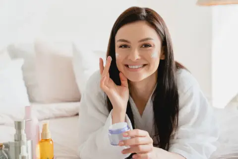 Donna sorridente applica crema viso, scoprendo i benefici di un siero probiotico per una pelle sana e luminosa.
