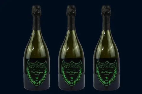 Trzy butelki szampana Dom Pérignon Vintage Brut w ciemnozielonych butelkach z czarnymi kapsułami i zielonymi etykietami.