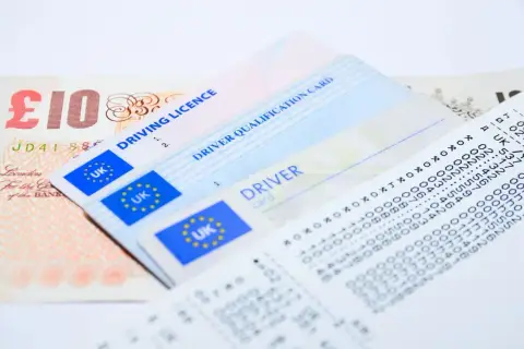 Brytyjskie prawo jazdy, karta kwalifikacji kierowcy i paragon obok banknotu 10 funtów. Wniosek o kartę kierowcy.