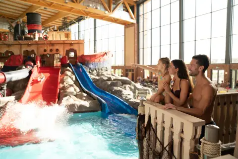 Familie genießt die **Therme mit Kindern**. Ein Junge rutscht auf einer roten Wasserrutsche, während die Familie zusieht.