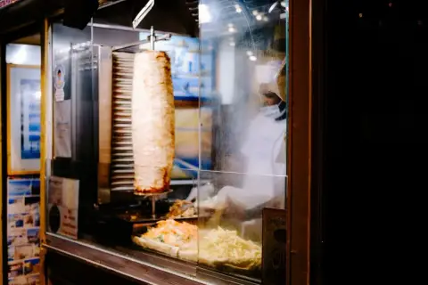 Obracający się pionowo kebab z frytkami i sałatką w witrynie.