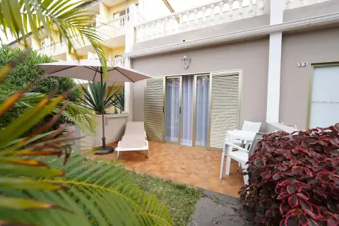 Terraza privada en el Hotel San Borondon con tumbona, sombrilla y mesa. Palmeras y vegetación exuberante rodean el espacio.