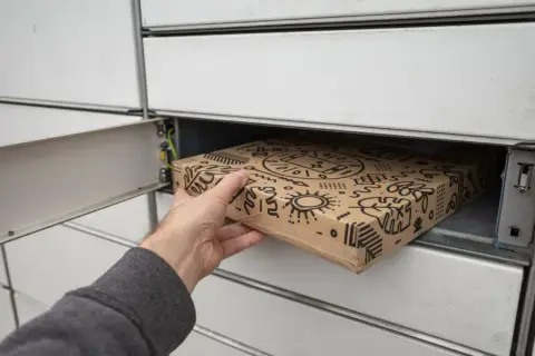 Dłoń wkłada paczkę z ozdobnym wzorem do skrytki paczkomatu.