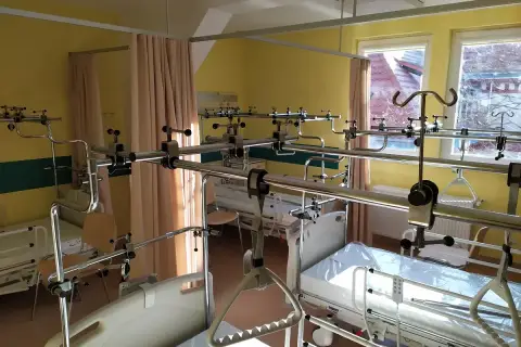 Pokój szpitalny z łóżkami i systemem poręczy nad łóżkami.