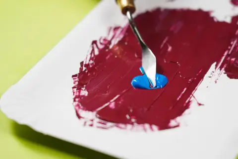 Mezclando azul con rojo para descubrir como se hace el color granate. Una espátula recoge pintura azul sobre una base roja.