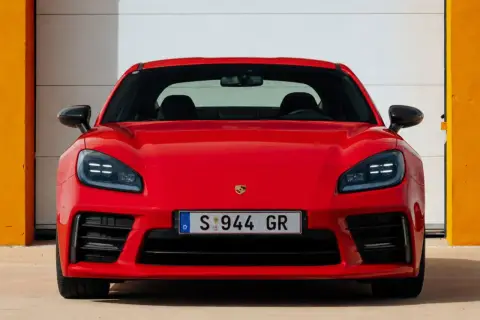 El llamativo Porsche 944 rojo, con su distintivo frontal y faros LED, se exhibe frente a una puerta de garaje blanca y paredes naranjas.