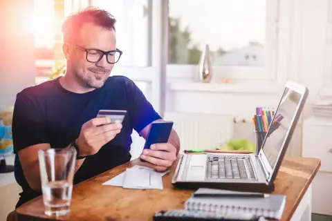 Mężczyzna z kartą płatniczą i telefonem w ręku, jakby planował zakupy. Nie ma tu żadnych provident złodziei, tylko domowe biuro.