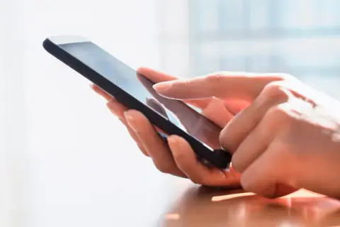 Dłoń dotyka ekranu smartfona, szukając archiwum SMS.