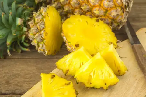 Soczyste kawałki ananasa na desce, obok całego owocu. Czy ananas jest zdrowy? Tak, to bomba witaminowa!