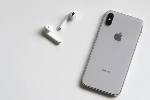 Srebrny iPhone i białe słuchawki AirPods leżą na białym tle. Może rozmówca na iPhonie słabo słychać?