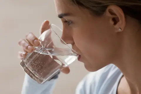 Kobieta pije wodę z kieliszka, wykonując test na odwodnienie.