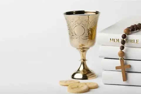 Złoty kielich, stos białych ksiąg z napisem "HOLY BIBLE", różaniec i opłatki. Symbolika sakramentu, który może być odnotowany w akcie chrztu.
