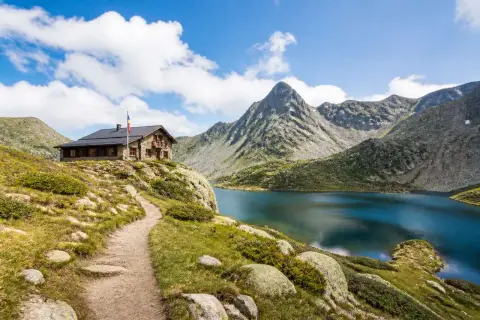 Sentier de randonnée en Andorre menant à un refuge de montagne près d'un lac alpin aux eaux bleues, avec des montagnes escarpées en arrière-plan.