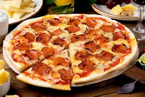 Pyszna pizza pepperoni z ciągnącym serem, obok serowe dodatki do pizzy, winogrona i kieliszek czerwonego wina.