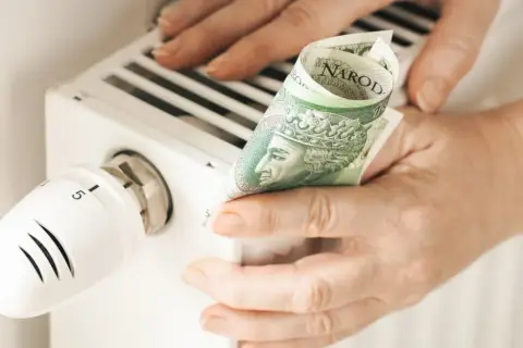 Ręce trzymają banknot 100 zł przy grzejniku. Sprawdzanie rachunków za ogrzewanie, cennik pogotowia gazowego.
