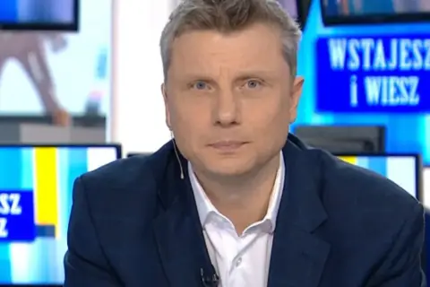 Rafał Wojda, wiek dziennikarza widoczny w jego spojrzeniu, w garniturze przed ekranem z napisem "Wstajesz i wiesz".