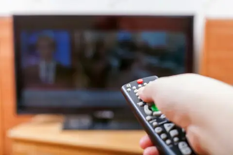 Dłoń z pilotem przed telewizorem, być może to już koniec abonamentu rtv i czas na zmiany.