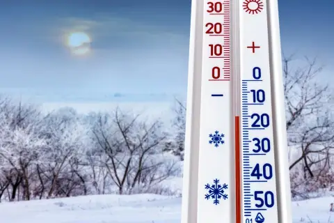 Termometr pokazuje -10°C, co zapowiada mroźną pogodę na styczeń 2026. Zimowy krajobraz z ośnieżonymi drzewami i bladym słońcem.