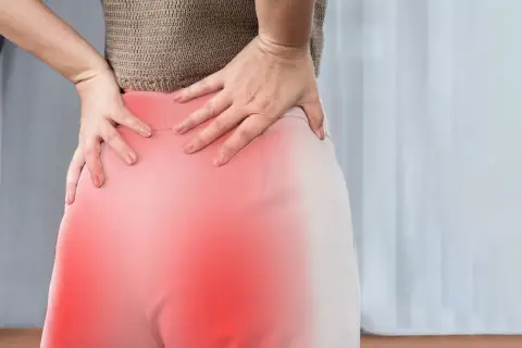 Kobieta trzyma się za bolące biodro, gdzie czerwony obszar sugeruje zapalenie korzonków.