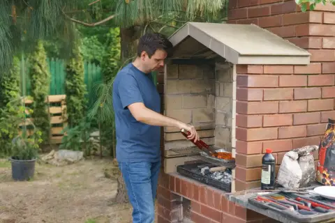 Mężczyzna grilluje mięso w ceglanym piecu. Wnętrze pieca wyłożone jest cegłami szamotowymi, które doskonale utrzymują ciepło.