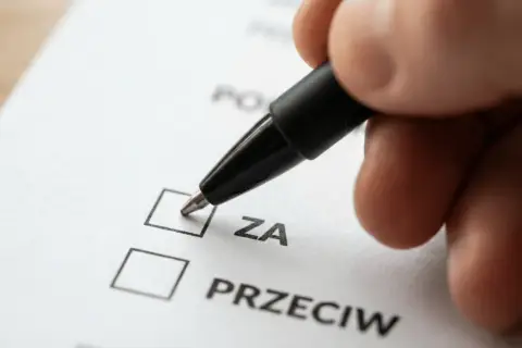 Dłoń z długopisem zaznacza opcję "ZA" na dokumencie. To ważny krok w zwołaniu zebrania wspólnoty mieszkaniowej przez właścicieli lokali.