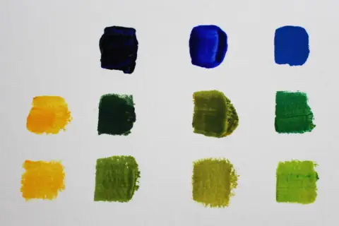 Farbproben auf weißem Papier: Blau, Dunkelblau, Gelb und verschiedene Grüntöne, die zeigen, wie man grün mischen kann.