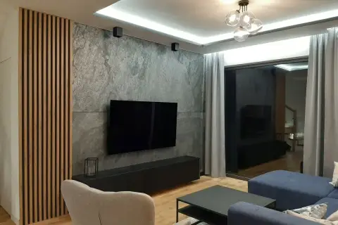 Nowoczesny salon z betonem architektonicznym, który świetnie komponuje się z drewnianymi lamelami i granatową sofą.