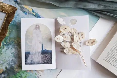 Otwarta księga z ilustracją postaci w bieli i suszonymi lunariami. Obok tekst, który może zawierać najpiękniejsze rozważania drogi krzyżowej.