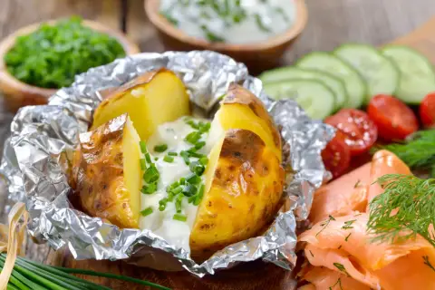 Pommes de terre à la braise, enveloppées dans du papier aluminium, garnies de crème et de ciboulette. Parfait pour le temps de cuisson.