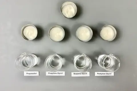 Sześć próbek kremów w małych pojemnikach i cztery zlewki z płynami: propanediol, glikol propylenowy, **butylene glycol** i pentylene glycol.