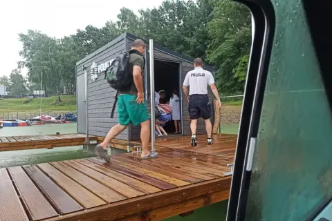 Policjanci na pomoście nad Soliną, przygotowani na nagłe zmiany pogody. Widać budynek z napisem "POLICJA" i łodzie w tle.